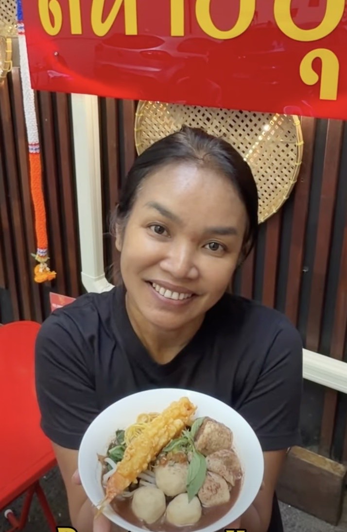 The owner of Say Hi smiling at the stall, holding a bowl of boat noodles